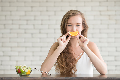 woman holding up an orange quarter with a salad in a bowl next to her