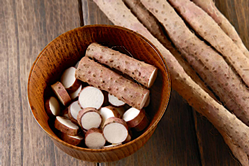 wild yam tubers in a bowl on a table next to a few more tubers laying next to it.