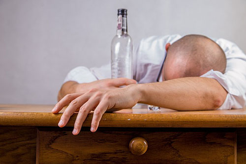 man slumped on a desk drunk and an empty liquor bottle in view