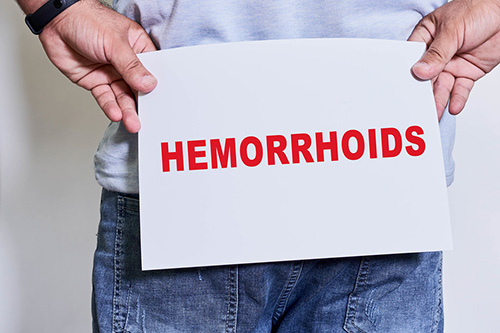 someone holding a sign that reads hemorrhoids behind their but