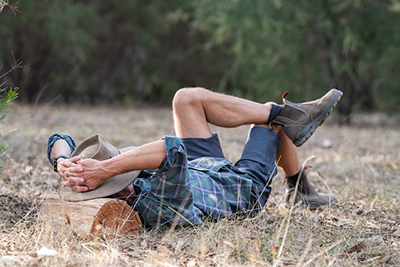 man taking a nap on the ground using a log as a pillow