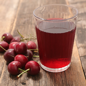 glass of cherry juice alongside a handful of cherries next to it
