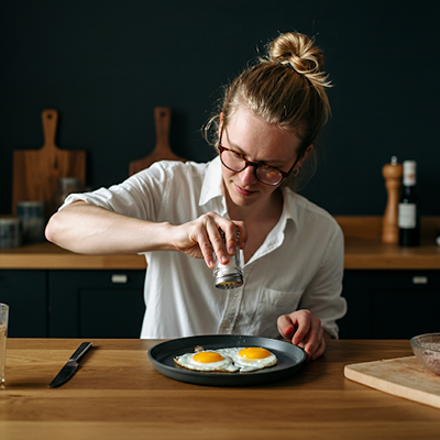 a woman putting salt (sodium) on eggs on a pan
